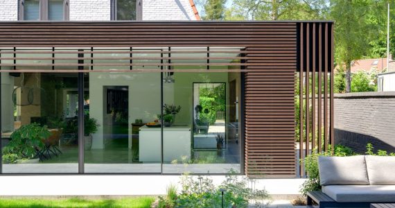 Foto van een moderne uitbouw aan een jaren '30 woning met houten lamellen op de gevel en grote glazen puien.