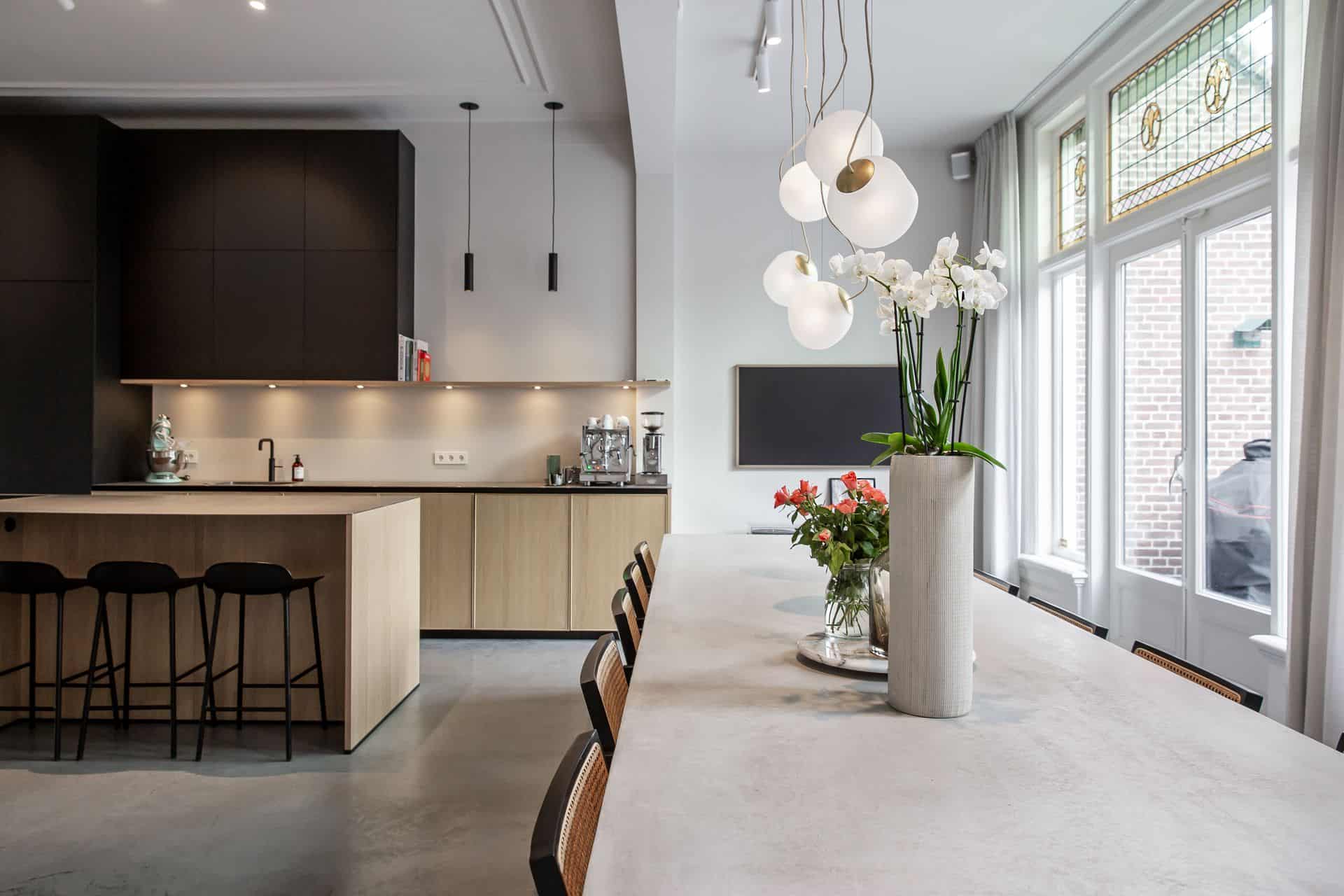 woonbeton van Willem Designvloeren in een moderne keuken in een herenhuis van de vorige eeuw gecombineerd met karakteristieke elementen zoals glas-in-lood ramen en sierlijsten aan het plafond.