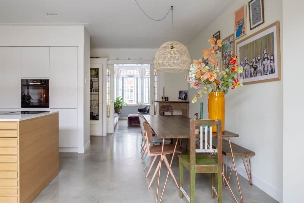 Betonnen gietvloer in een karakteristieke woning in Haarlem, met gekleurde stoelen aan de eettafel en een wit met houten keuken.