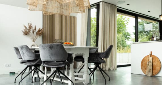 Woning in Nuenen met een gevlinderde betonvloer van Willem Designvloeren. Hierop staat een witte eettafel met daaraan grijze stoelen. Ook staat er een wit kookeiland op de gevlinderde betonvloer.