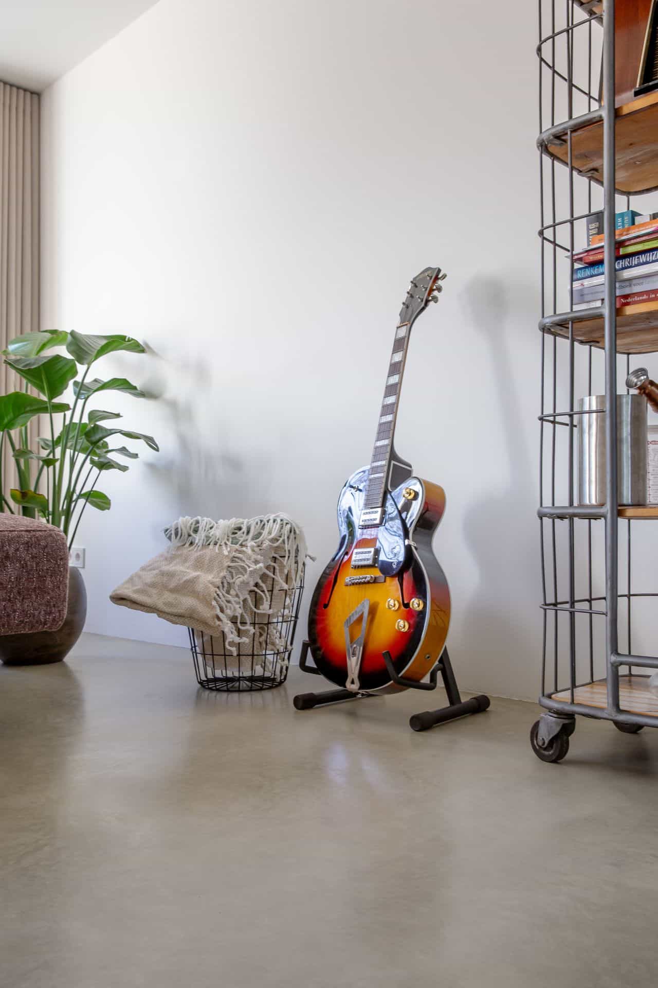 Gevlinderde betonvloer in Sprang-Capelle. Hierop staat een gitaar en een mand met een kleed daarin.