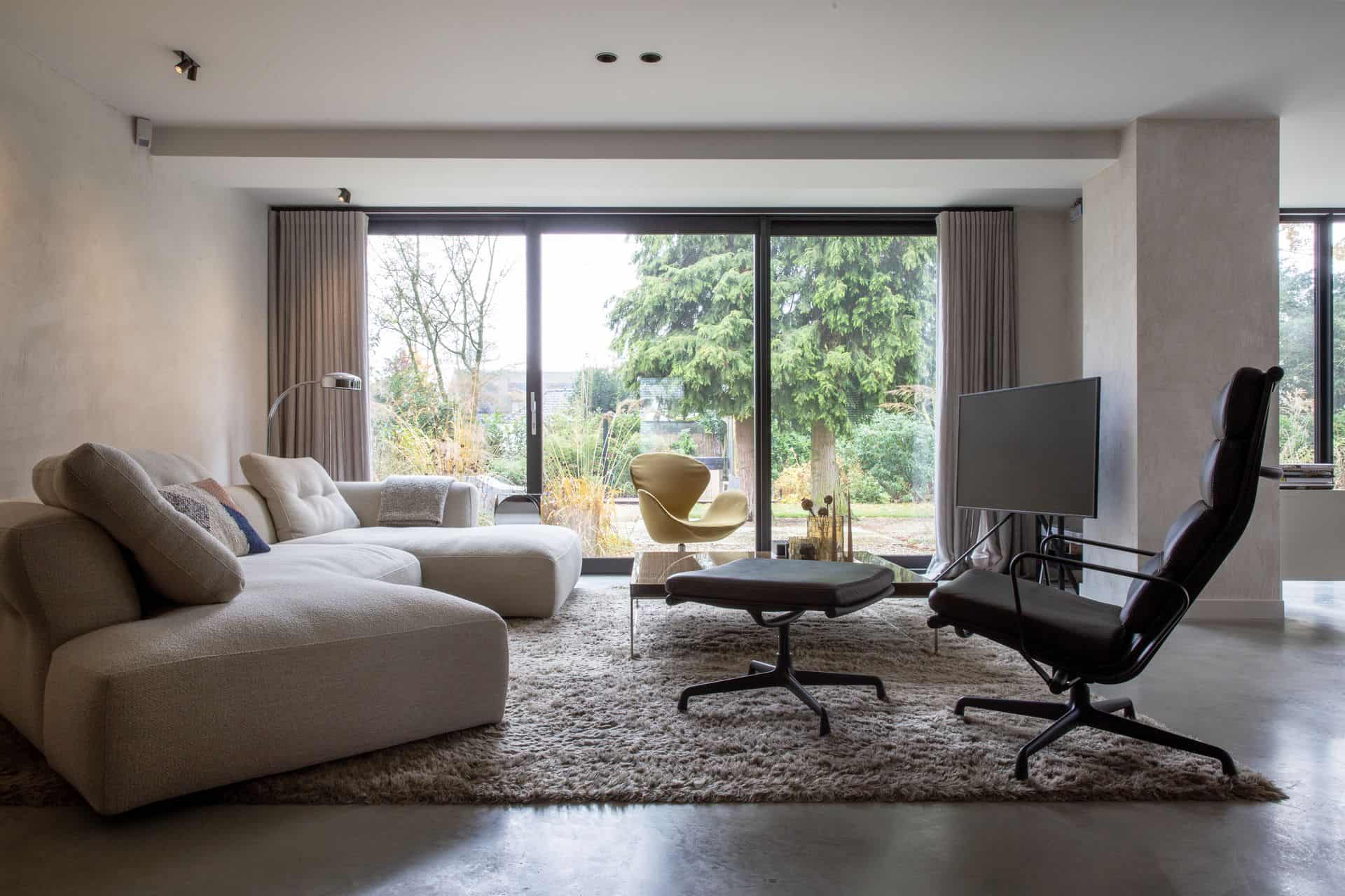 Woonkamer in Waalwijk met een beige bank, licht kleed, zwarte en gele stoel. Dit alles staat op een gevlinderde betonvloer.