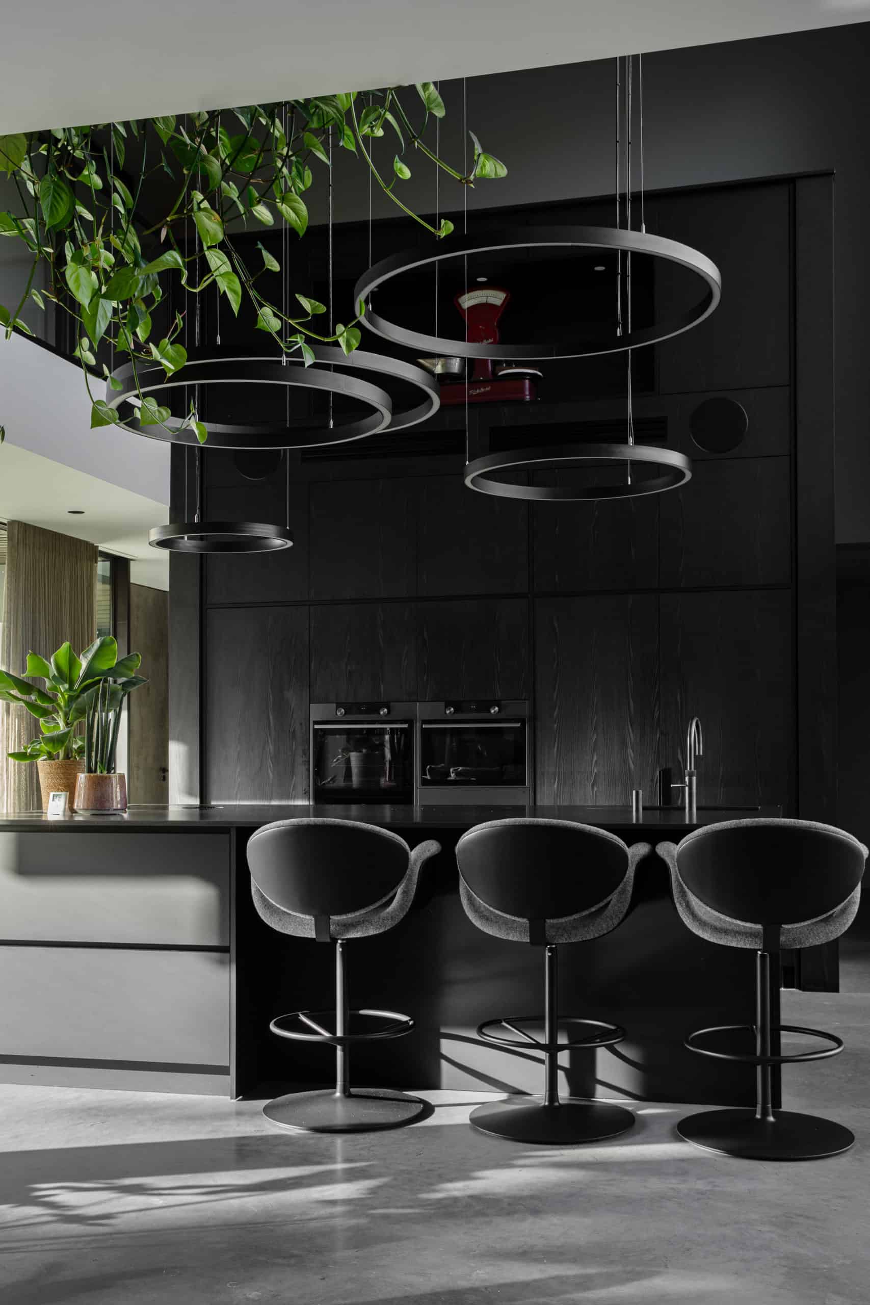 Villa woning in Bemmel met een gevlinderde betonvloer van Willem Designvloeren gecombineerd met een zwarte keuken en een zwart kookeiland met hieraan 3 barkrukken.