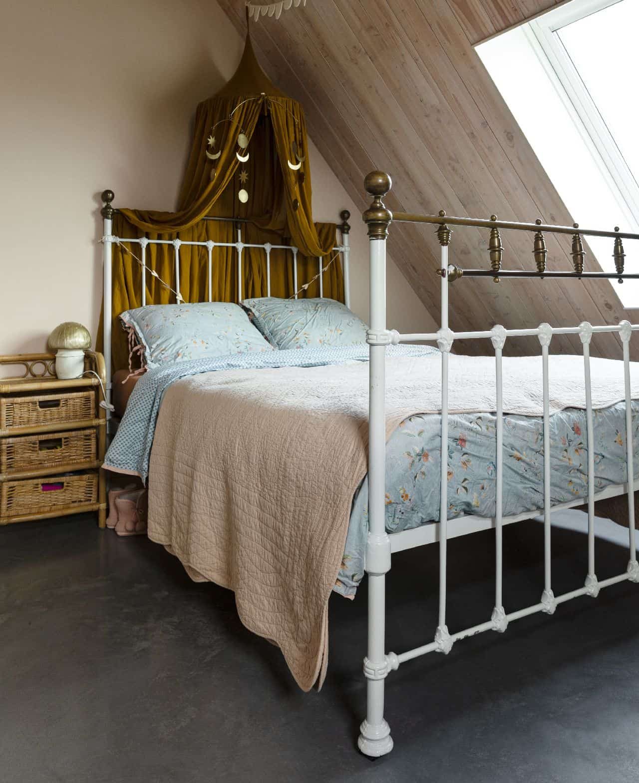 Vrijstaande woning in Brandwijk met een gevlinderde betonvloer in de slaapkamer. Hierop staat een wit bed met een blauw dekbedovertrek en er hangt een geel-groene klamboe.