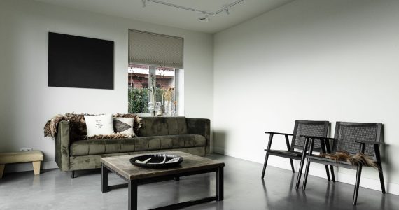 Vrijstaande woning in Brandwijk met een gevlinderde betonvloer in de woonkamer. Hierop staat een groene velvet bank en twee zwarte stoelen.