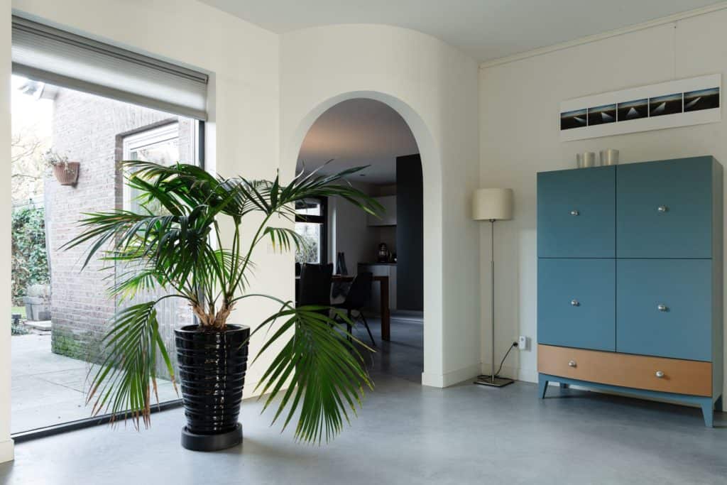 Woning in Rosmalen. Hierin ligt een gevlinderde betonvloer. Op de betonvloer staat een plant in een zwarte pot. Je kijkt door naar de keuken. Deze zit achter een ronde doorgang.