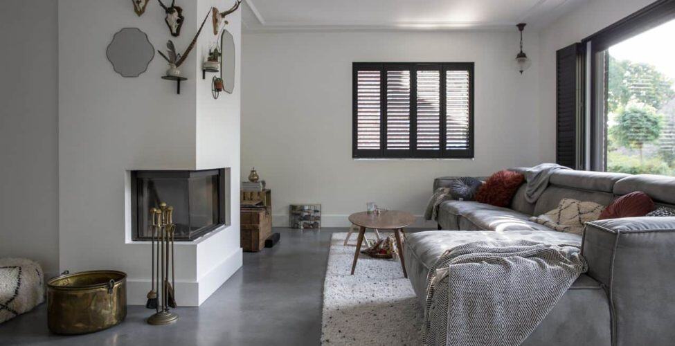 Gevlinderde woonbeton vloer in de woonkamer in Tilburg met daarop een wit vloerkleed en een grijze bank.