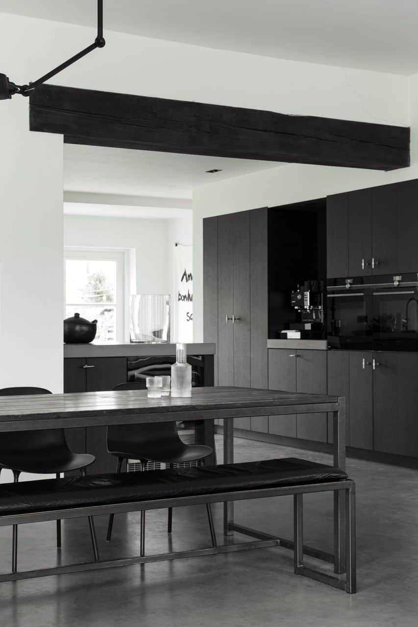 Zwarte houten keuken in Gieterveen met een houten tafel en hieraan zwarte stoelen. Gecombineerd met een gevlinderde betonvloer.