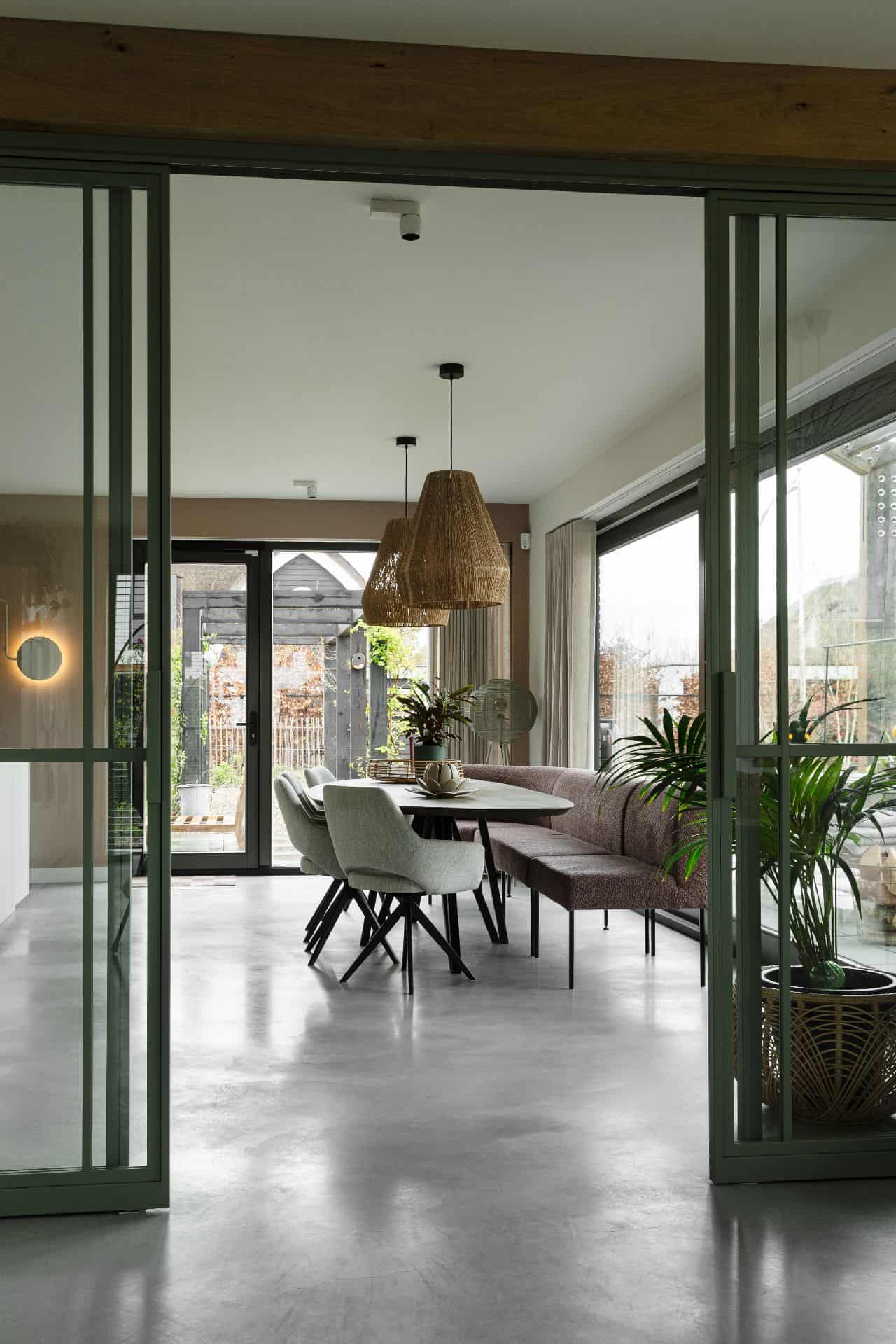 Eetkamer in Veenendaal met een zwarte tafel en daaraan grijze stoelen en een roze bankje. Dit staat op een gevlinderde betonvloer.