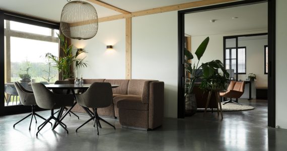 Gevlinderde betonvloer en betonnen terras in Zeist hierop staat een zwarte eettafel met daaraan een bruine bank en grijze stoelen.