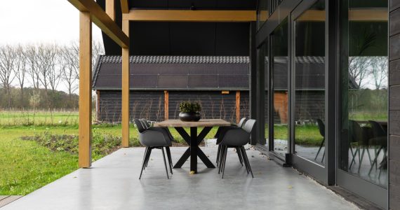 Gevlinderde betonvloer en betonnen terras in Zeist. Op het terras staat een houten tafel met zwarte poten en daaraan zwarte stoelen.