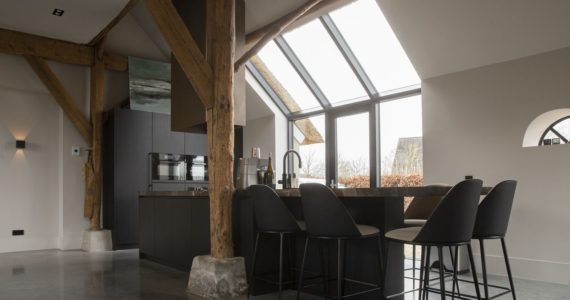 Gevlinderde betonvloer in de keuken in Ochten. De keuken is zwart met een marmeren blad. Aan het kookeiland staat zwarte barkrukken.