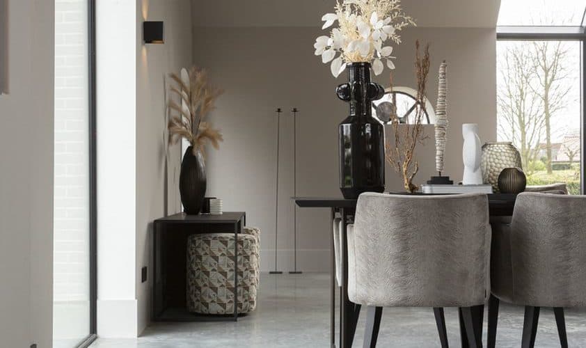 Gevlinderde betonvloer in een woning in Ochten gecombineerd in een landelijk interieur met een zwarte eettafel en daaraan grijze stoelen.