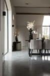 Gevlinderde betonvloer in een woning in Ochten gecombineerd in een landelijk interieur met een zwarte eettafel en daaraan grijze stoelen.