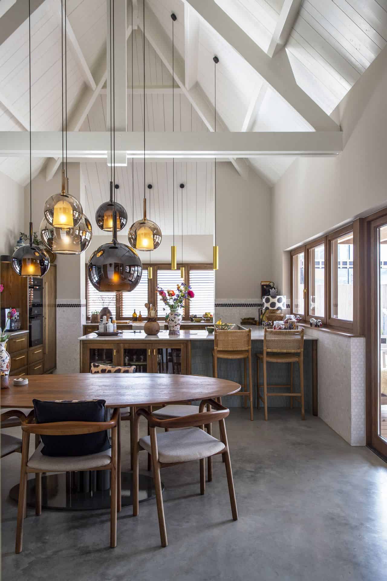 Keuken in Ulvenhout waarbij er veel gebruik gemaakt is van houten elementen. Zo is de keuken van hout, de ronde eettafel van hout en de stoelen en de barkrukken zijn ook van hout. Dit is gecombineerd met een gevlinderde betonvloer. De keuken heeft een hoog wit plafon wat in een punt loopt, hieraan hangen lange, ronde lampen. Beton laten storten kosten