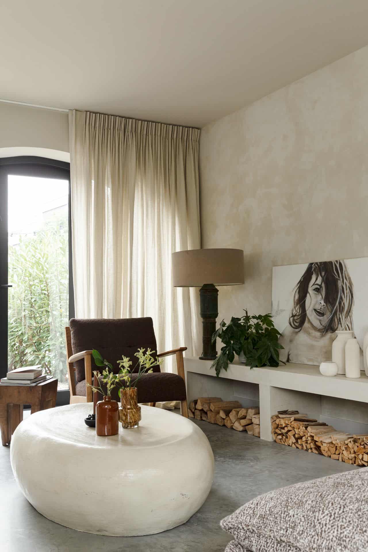 Woonkamer met een gevlinderde betonvloer en zandkleurige wanden in Rijnsburg. Hierop staat een houten stoel en tafeltje en een wit rond tafeltje.