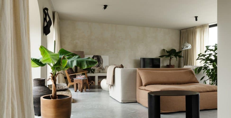 Woonkamer in Rijnsburg. Hierin ligt een gevlinderde betonvloer en dit is gecombineerd met veel houten en beige details.