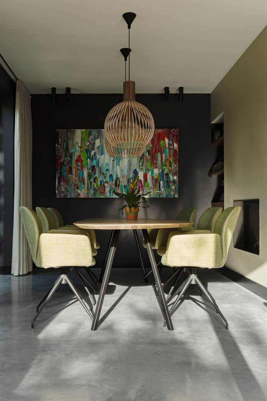 Houten eettafel met zwarte poten en daaraan groene stoelen in Venlo. Dit staat op een gevlinderde betonvloer. Aan de zwarte wand hangt een gekleurd schilderij.