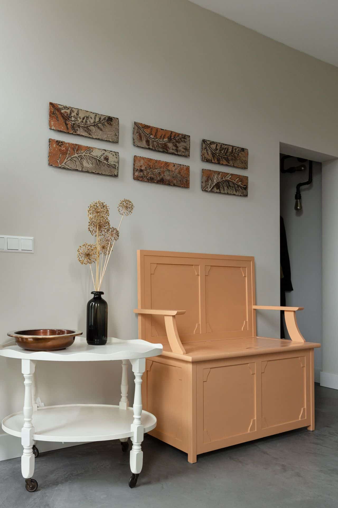 Woning in Woudenberg met een gevlinderde betonvloer. Hierop staat een wit tafeltje en een oranje kast. Hierboven hangen wat schilderijtjes aan de wand.