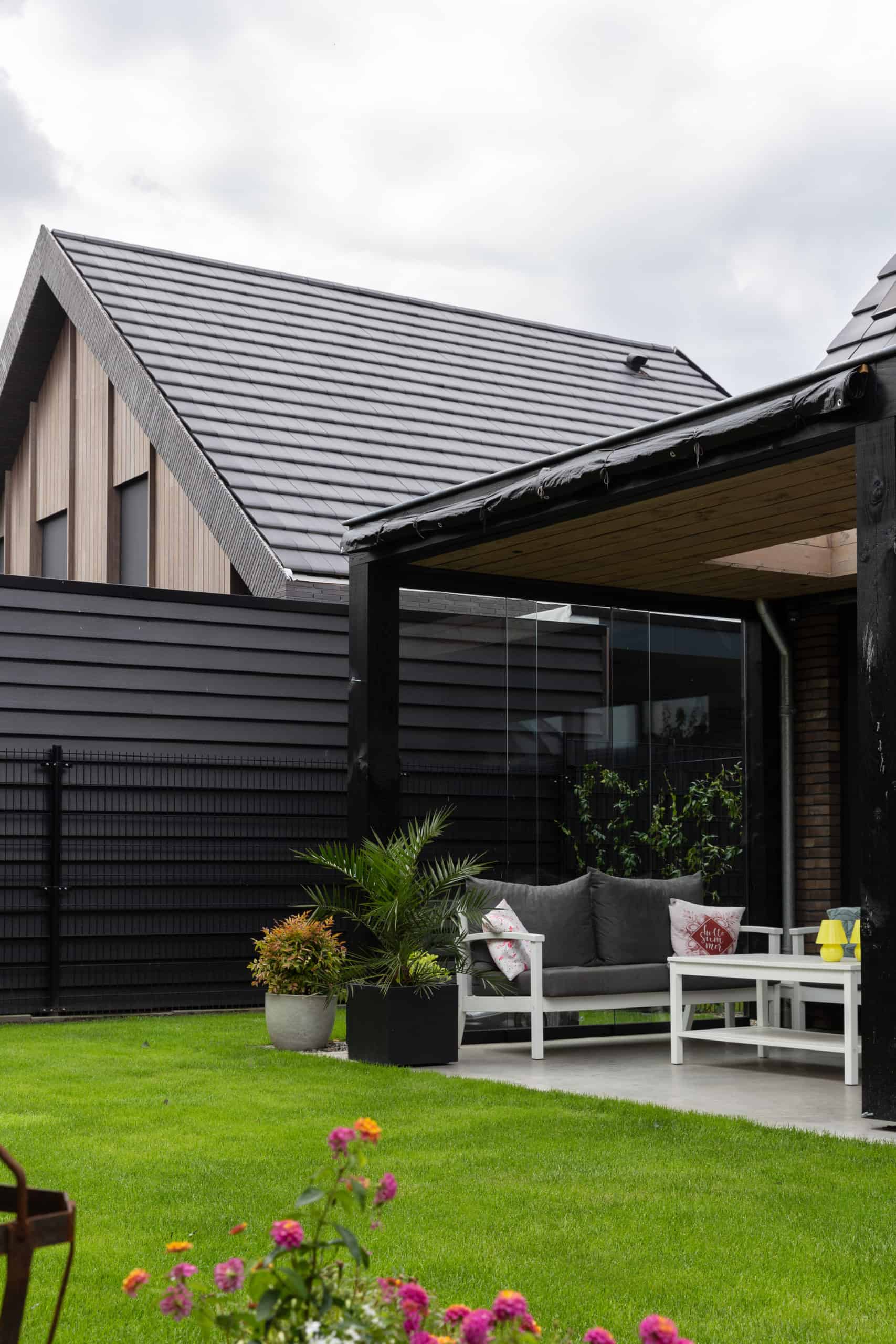 Terras onder een overkapping in Hilvarenbeek. Deze is gecombineerd met gras en op het terras staat een wit tuinset met grijze stoelen.