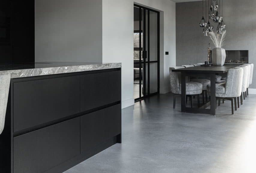 Grijze Italiaanse betonlook vloer in de kleur Rome gelegd in de landelijke keuken in Opheusden. Hierop staat een zwart kookeiland, met een grijs marmeren blad. En een zwarte tafel met daaraan grijze stoelen.