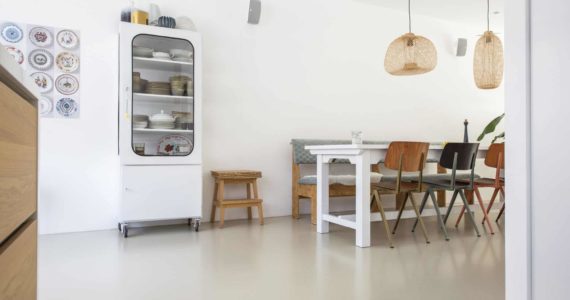PU gietvloer van Willem Designvloeren in Zeist. Hierop staat een witte eettafel met daaraan houten stoelen en een houten bank.