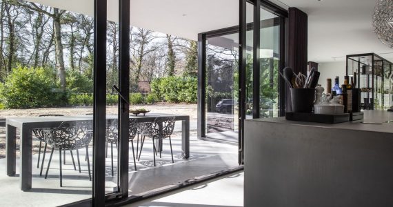 Gevlinderde betonvloer en een gevlinderd betonnen terras in Nijmegen met een grijs kookeiland op de binnenvloer en op de buitenvloer staat een grijze tafel.