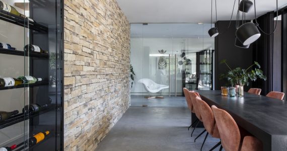 Gevlinderde betonvloer van Willem Designvloeren gecombineerd met een stenen muur en op de vloer staat een zwarte tafel met bruine stoelen.