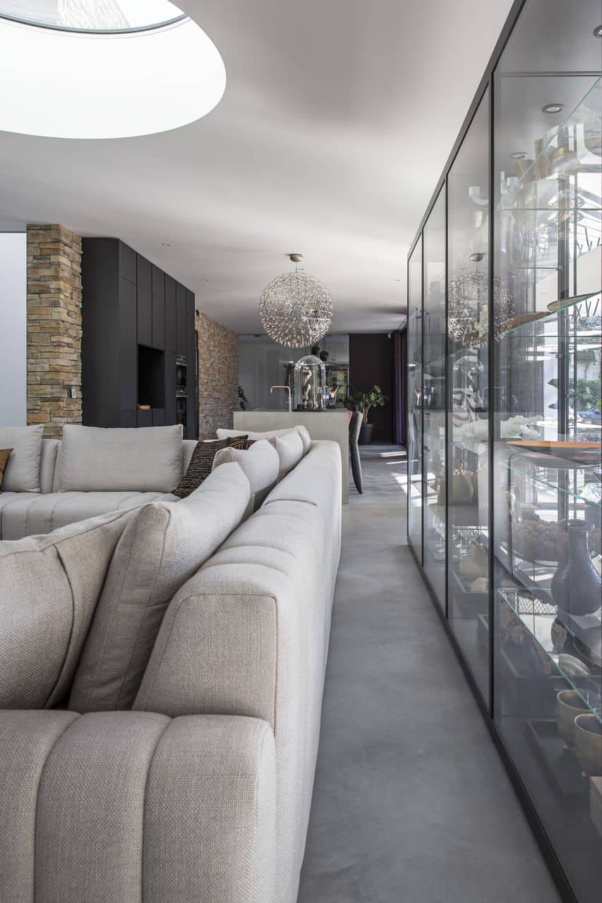 Gevlinderde betonvloer in de woonkamer in Nijmegen met daarop een beige bank en een glazen kast.