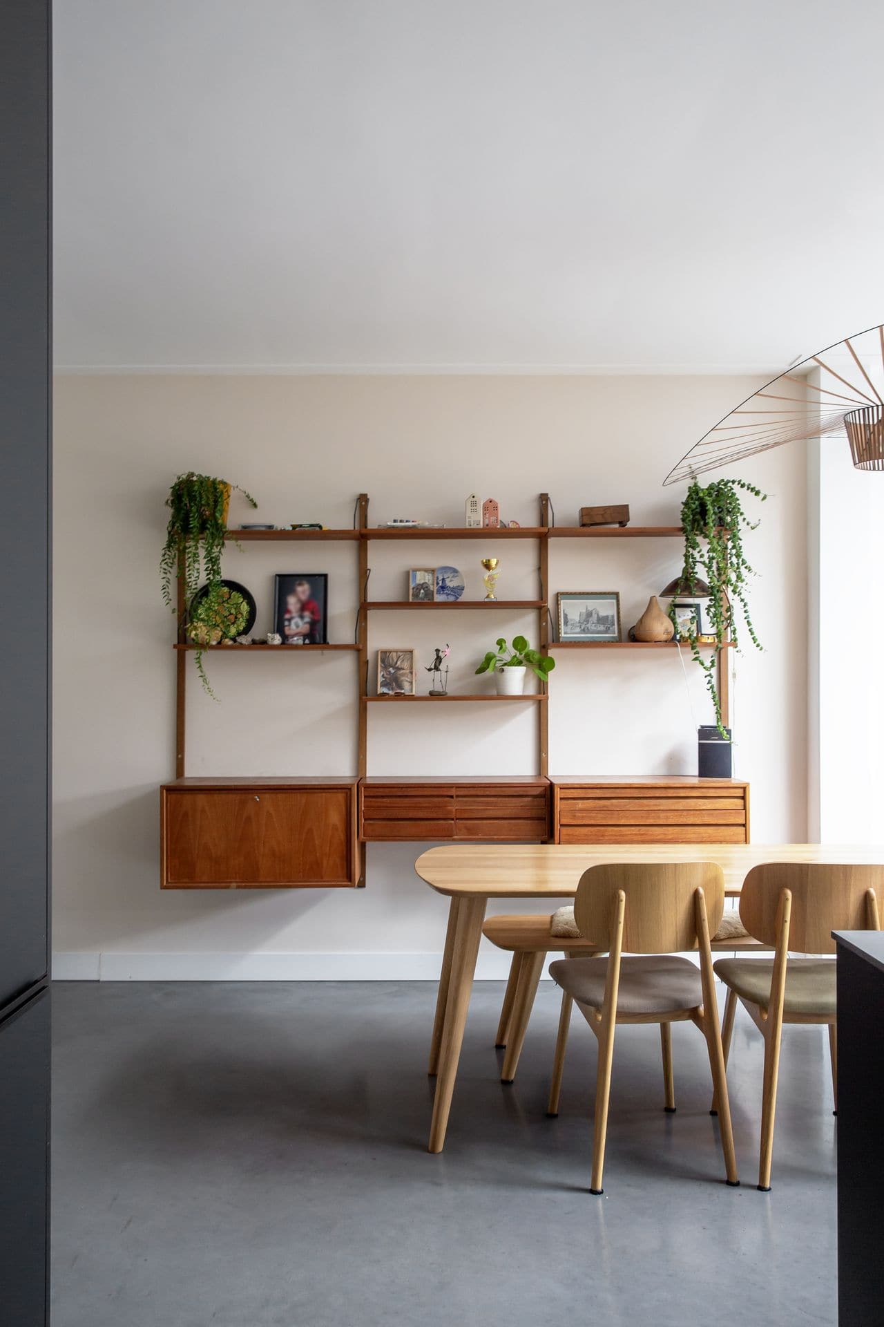 Woning in Haarlem met een gevlinderde betonvloer. Hierop staat een houten tafel met houten stoelen en aan de wand hangt een houten kastje.