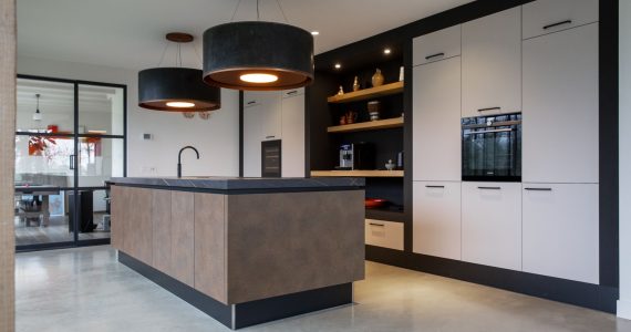 Witte keuken met een bruin kookeiland in Lewedorp. Gecombineerd met een gevlinderde betonvloer en grote zwarte lampen.