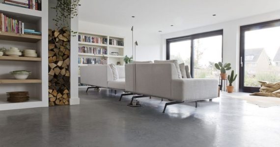 Gevlinderde betonvloer van Willem Designvloeren in de woonkamer met op de vloer een beige bank.