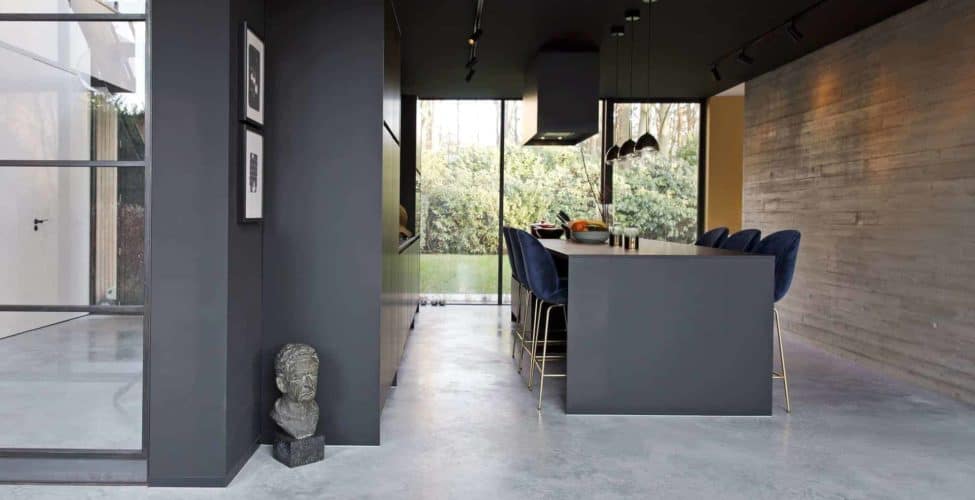 Gevlinderde betonvloer in de keuken in Huizen met daarop een zwarte keuken en een zwart kookeiland met daaraan blauwe barkrukken met gouden poten.