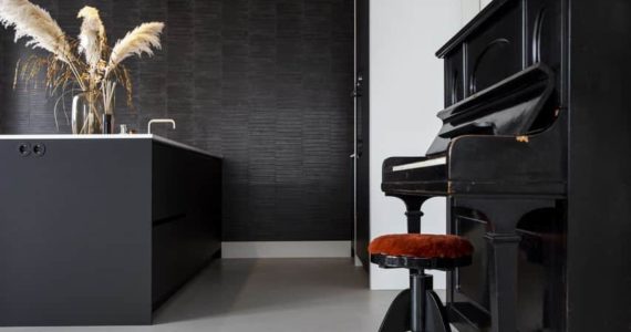 Beton ciré vloer in de keuken gecombineerd met een zwart kookeiland en een zwarte piano.