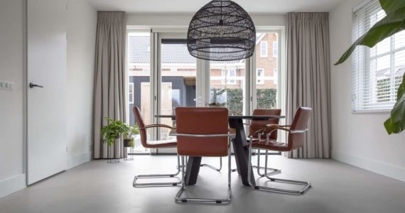 Beton ciré vloer in de eetkamer in Kesteren. Hierop staat een zwarte eettafel met daaraan oranje stoelen.