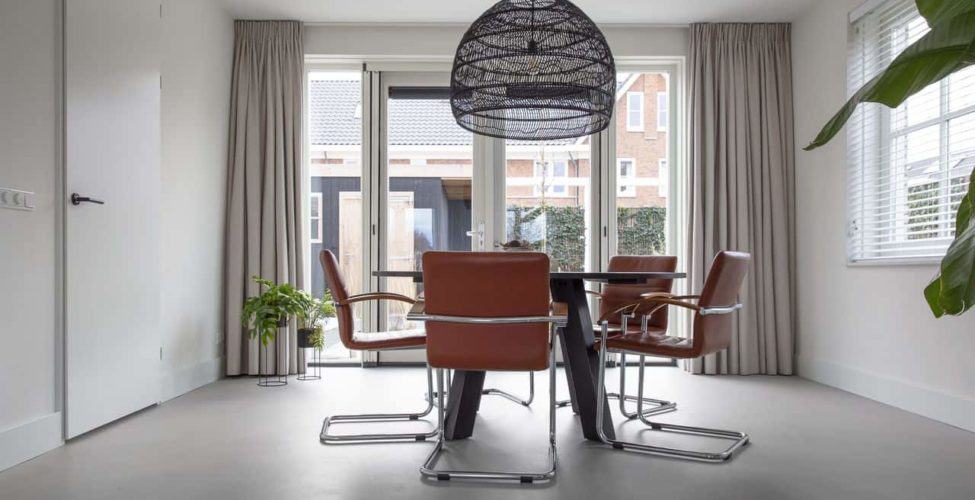 Beton ciré vloer in de eetkamer in Kesteren. Hierop staat een zwarte eettafel met daaraan oranje stoelen.