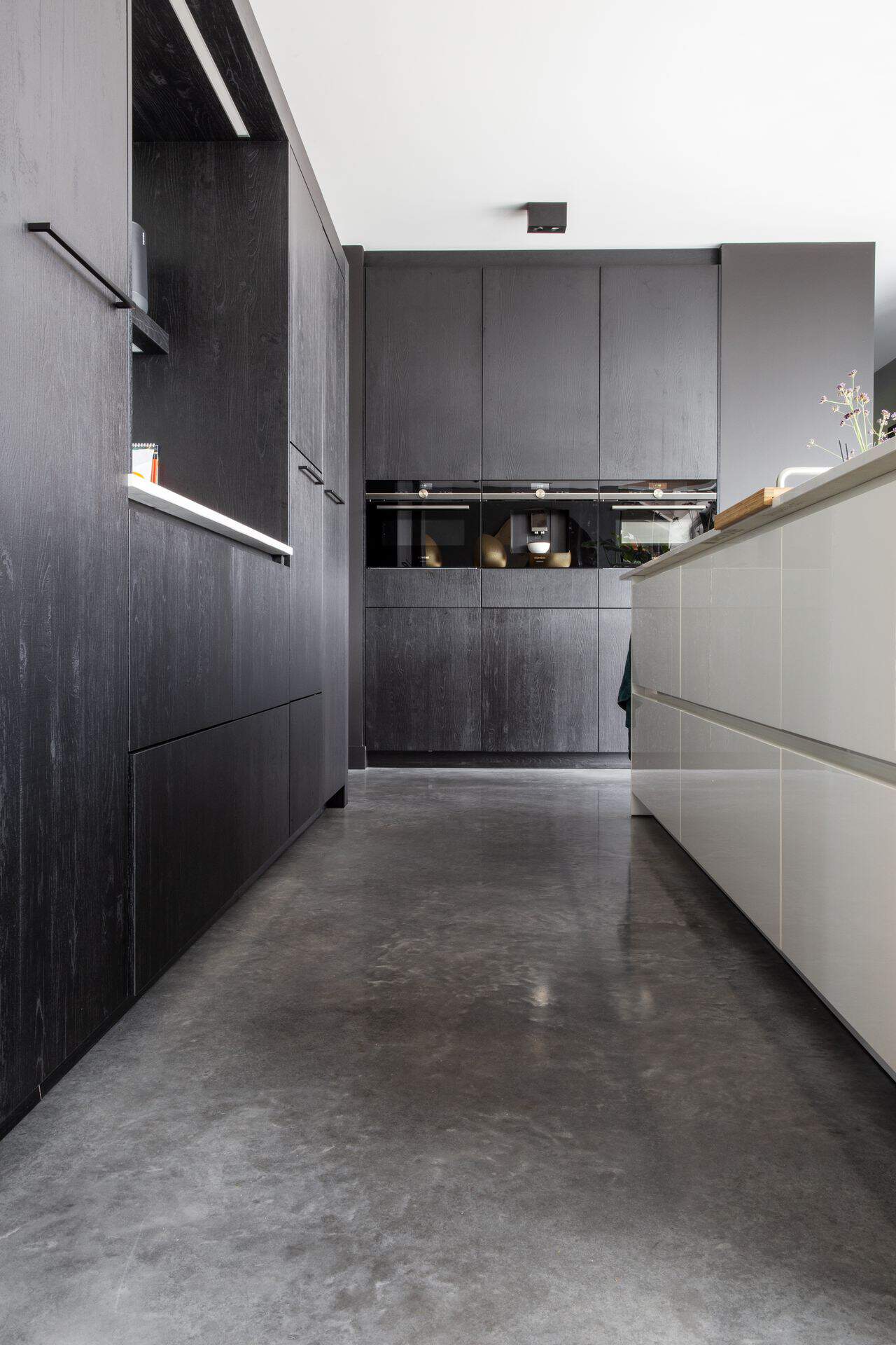 Zwarte keuken in Nuenen met een wit kookeiland. Hierbij ligt een gevlinderde betonvloer.