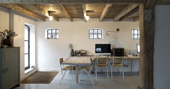 Gevlinderde betonvloer in gerenoveerde boerderij met een houten tafel en hieraan witte stoelen.
